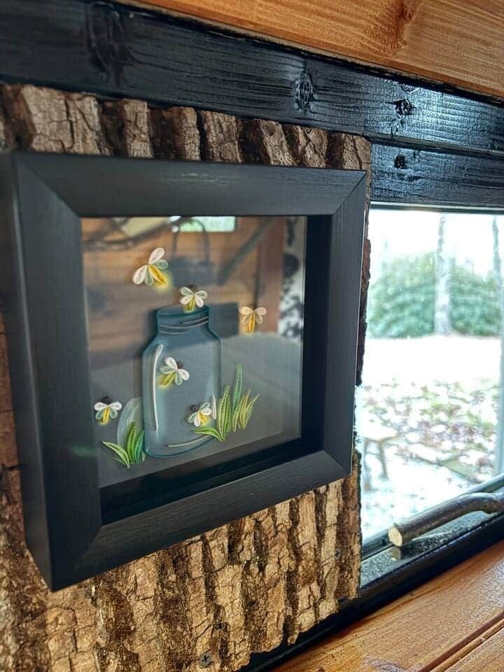 A picture of a mason jar with bees in it is hanging on a wooden wall.