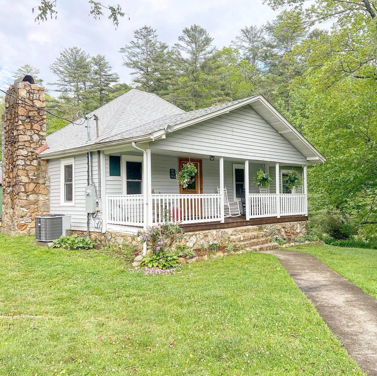 A small white house with a porch and a stone chimney.