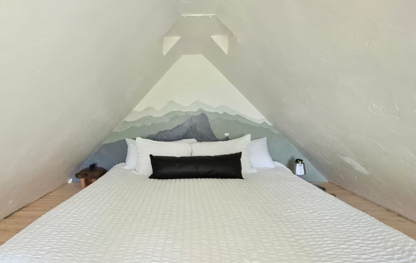 There is a bed in the attic with mountains painted on the wall.