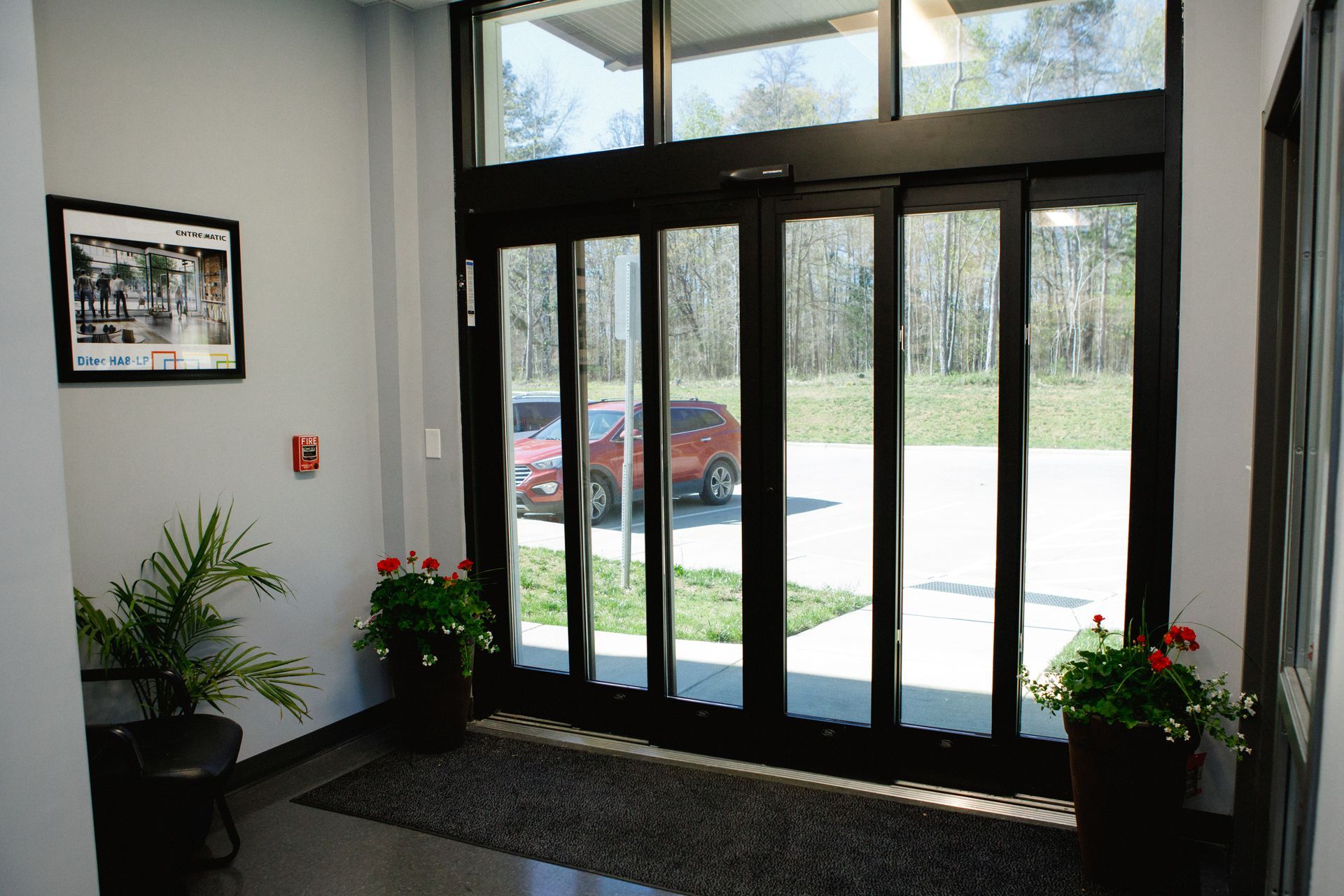 Hall d'entrée avec portes vitrées, plantes en pot et vue sur les voitures garées à l'extérieur