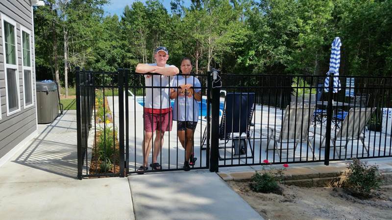 man and women standing at wrought iron gate inside pool area