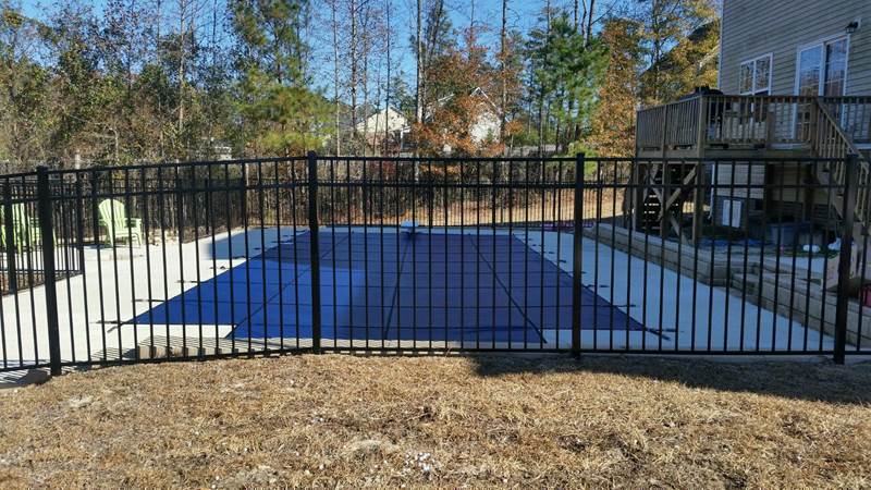 safety cover on inground pool inside black wrought iron fence