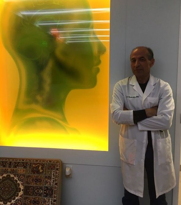 A man in a lab coat stands in front of a painting of a woman 's head