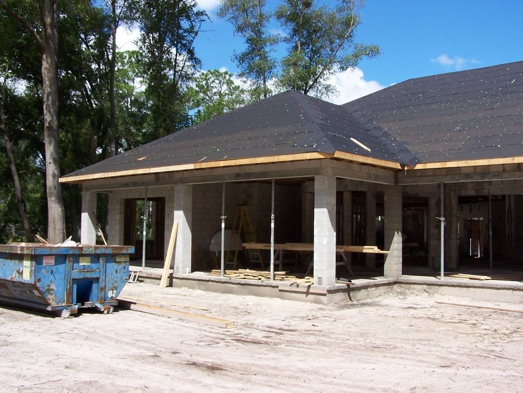 A blue dumpster sits in front of a house under construction