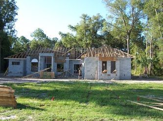 A house is being built in a grassy area with trees in the background