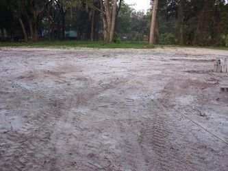 A muddy field with trees in the background and tire tracks in the dirt.