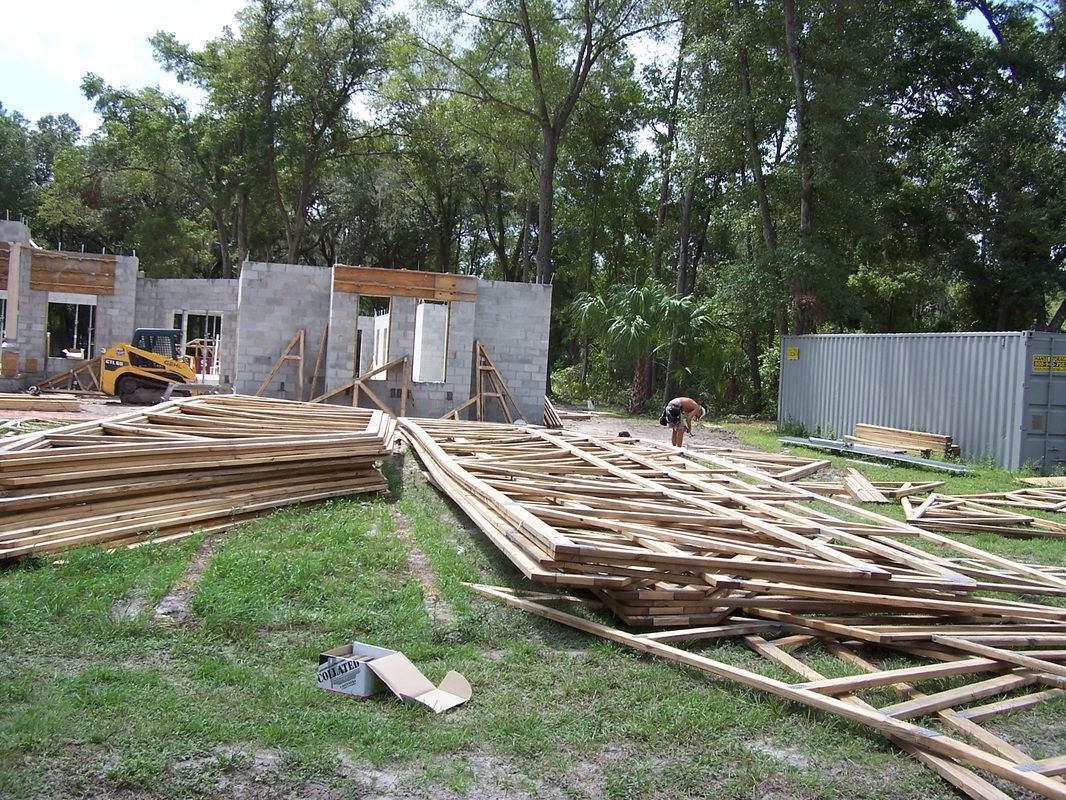 A pile of wood is sitting in the grass in front of a building under construction.