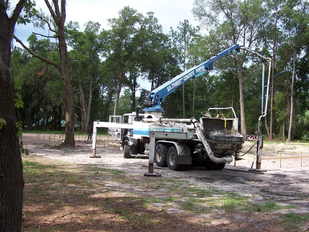 A concrete pump truck is parked in a dirt field with trees in the background.