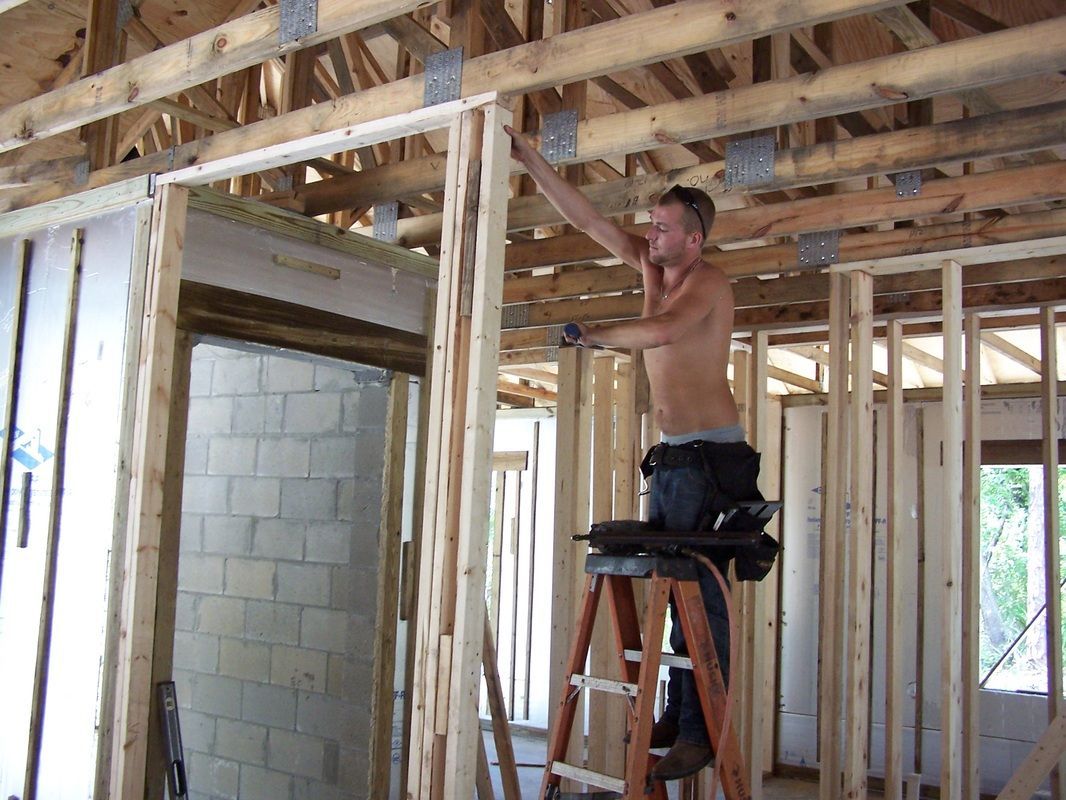 A shirtless man is standing on a ladder in a house under construction.