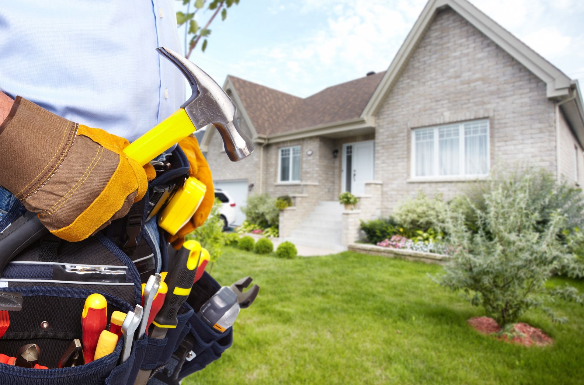 A man is holding a hammer and tools in front of a house.