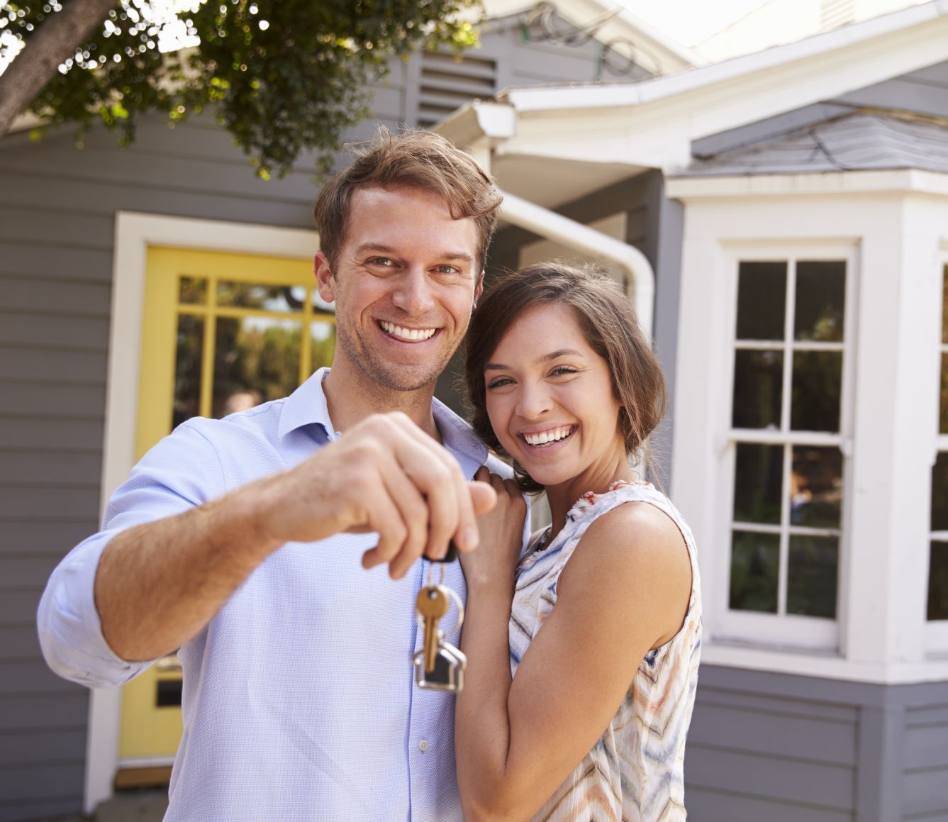 A man and woman holding keys in front of a house