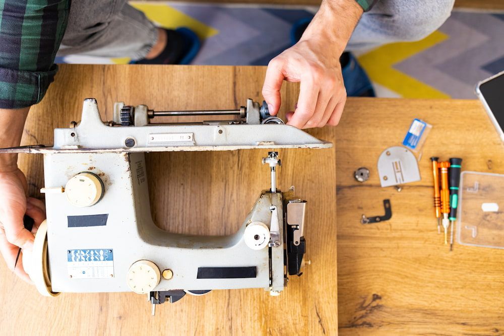 A Man is Fixing a Sewing Machine on a Wooden Table — James Hunter Mobile Sewing Machine Mechanic in Caloundra, QLD