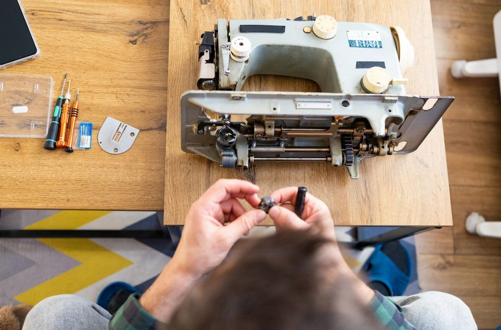 A Man is Fixing a Sewing Machine on a Wooden Table — James Hunter Mobile Sewing Machine Mechanic in Battery Hill, QLD