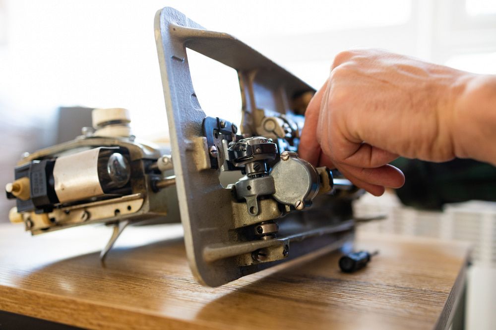 A Person is Fixing a Machine on a Wooden Table — James Hunter Mobile Sewing Machine Mechanic in Battery Hill, QLD