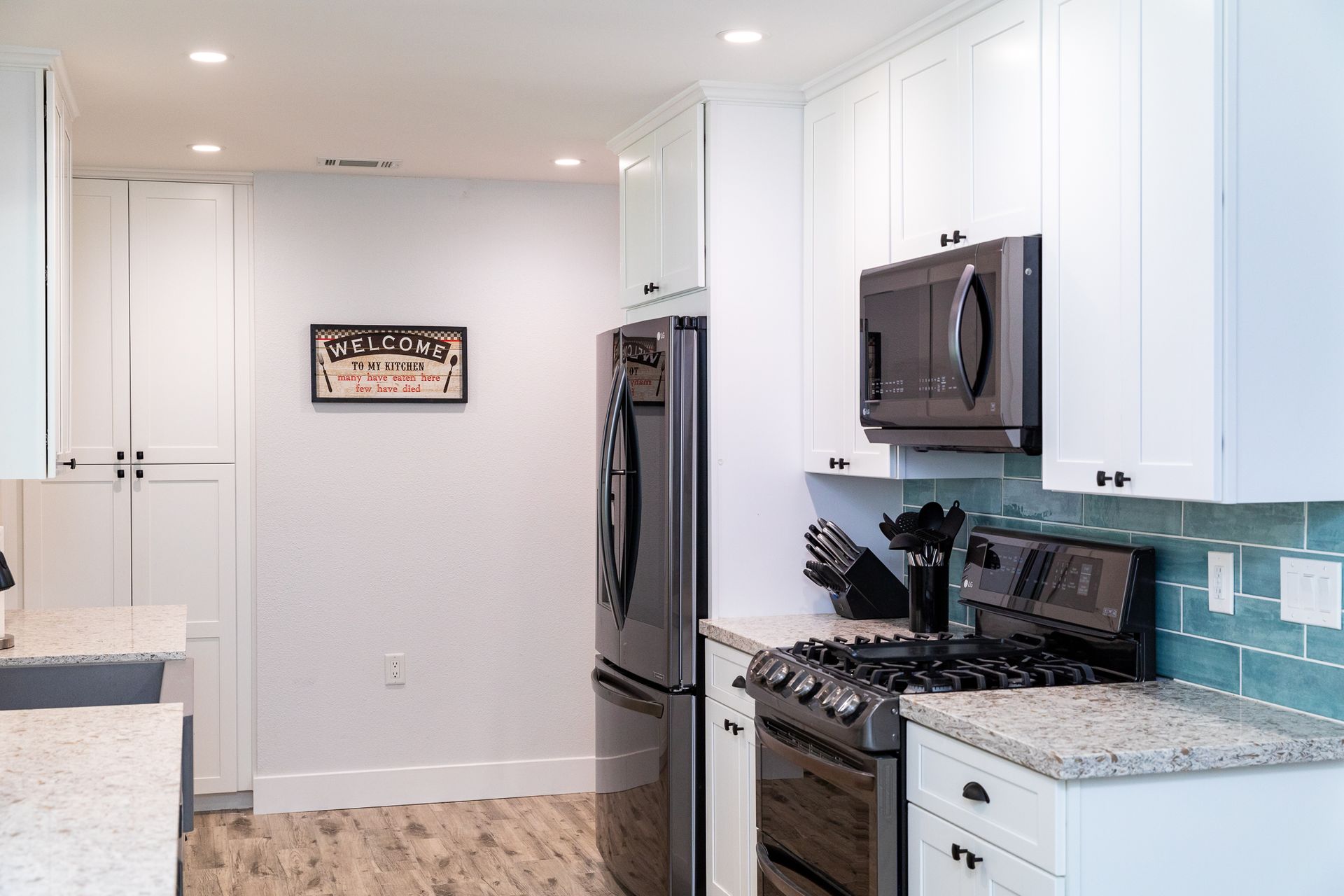A kitchen with white cabinets , a stove , a refrigerator , and a microwave.