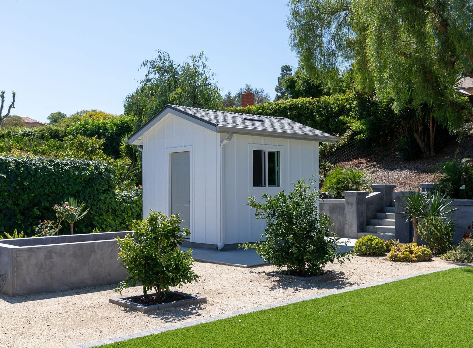 A small white shed is sitting in the middle of a lush green yard.