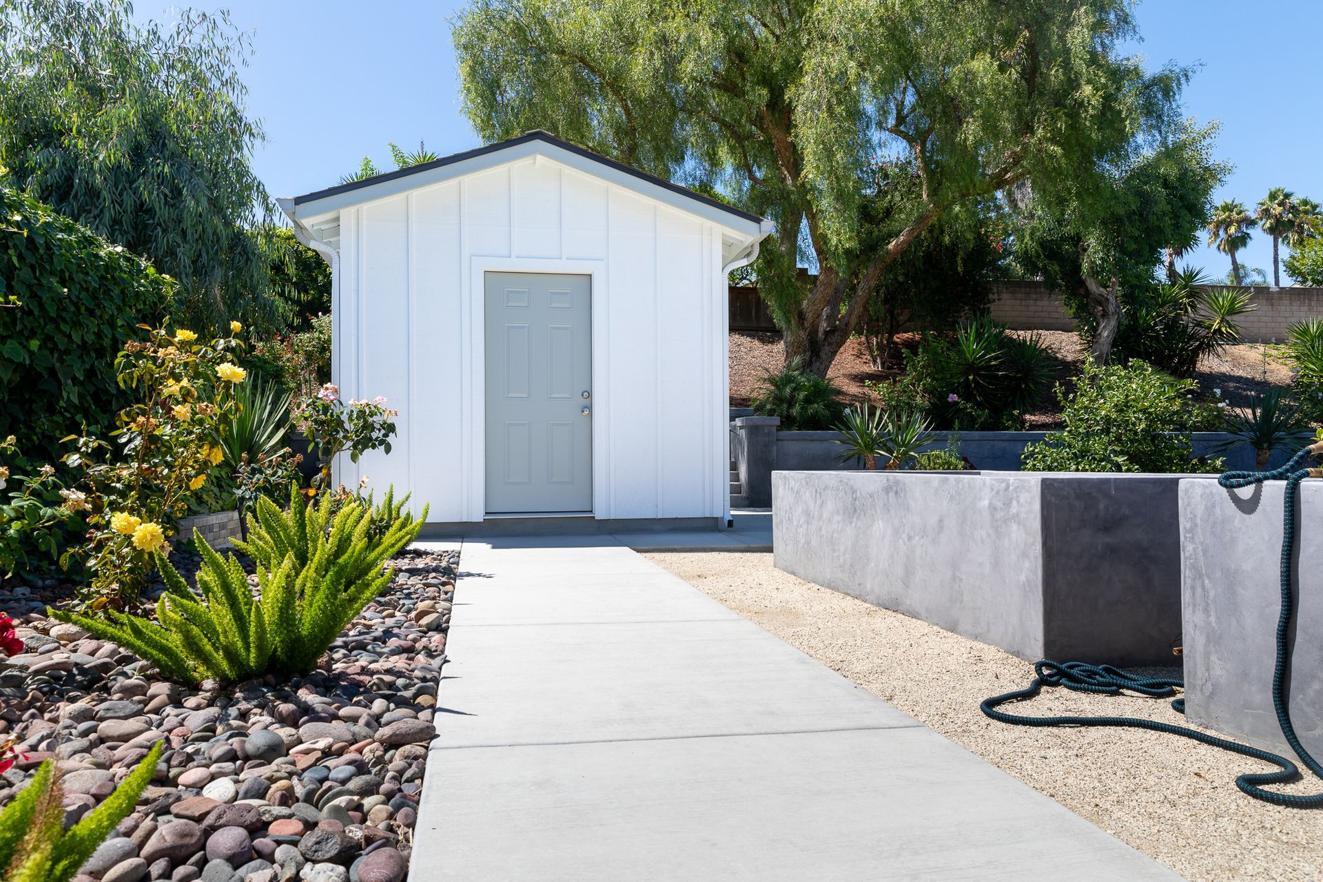 A small white shed is sitting in the middle of a rocky yard.