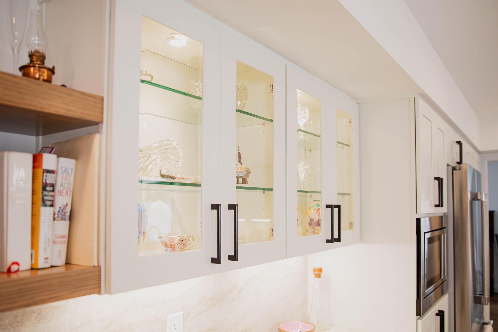 White kitchen cabinets with glass doors, illuminated interior, black hardware.