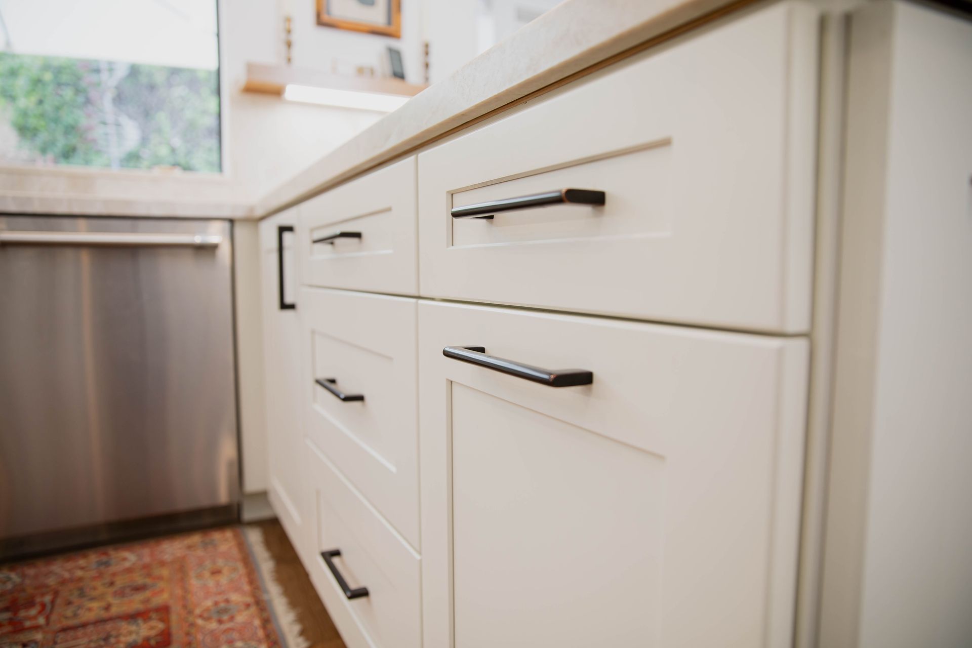 A kitchen with white cabinets and black handles and a stainless steel dishwasher.