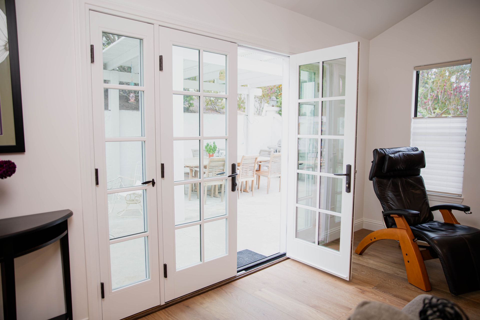 A living room with french doors open and a chair.