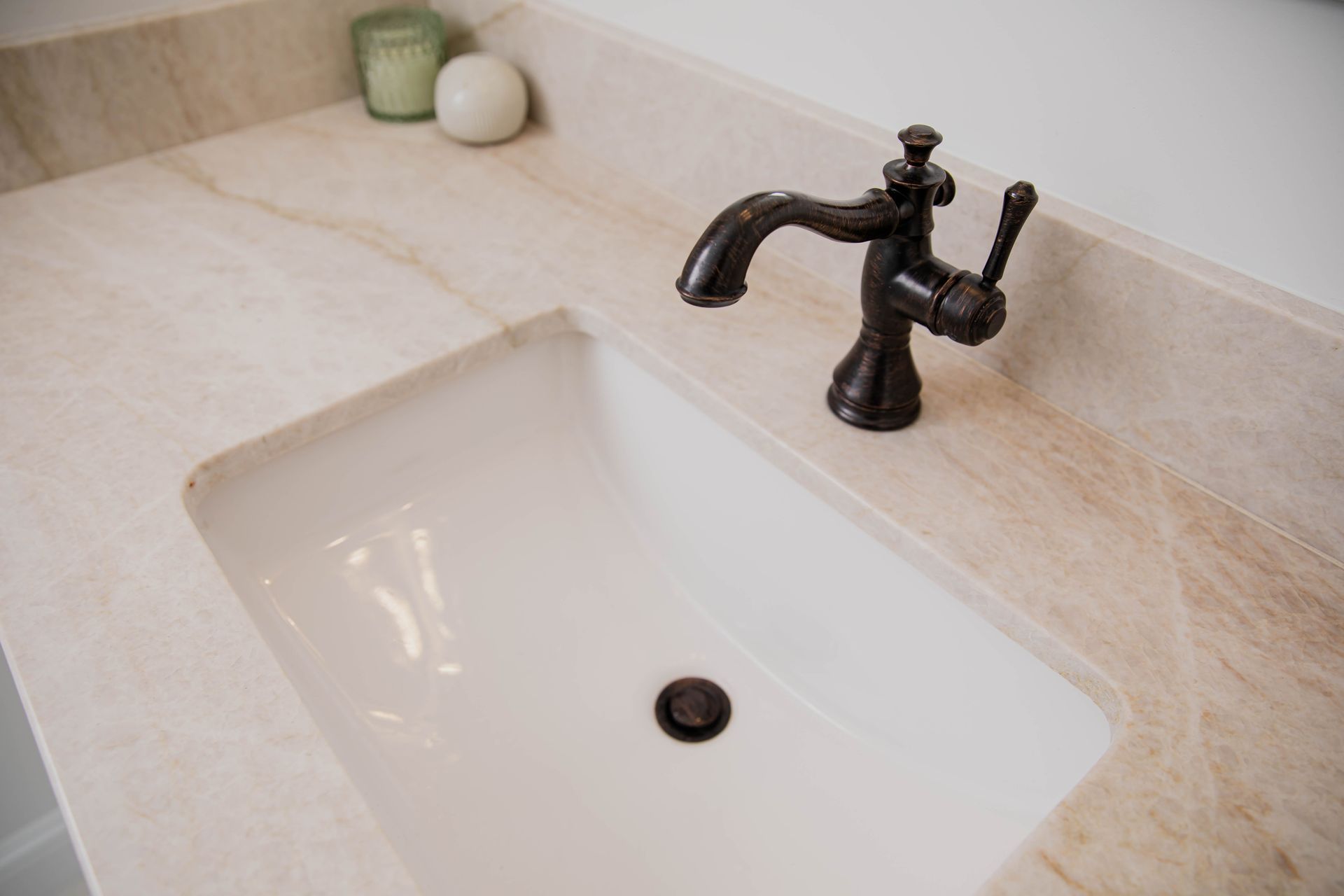 A bathroom sink with a brown faucet and a candle on the counter.