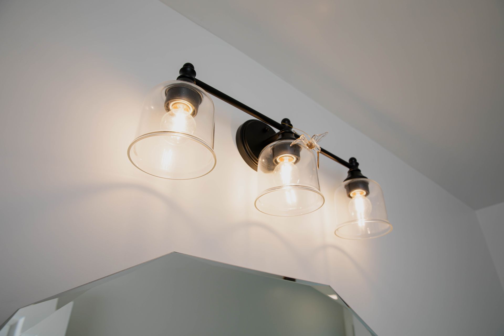 A bathroom vanity light with clear glass shades is hanging on a white wall.