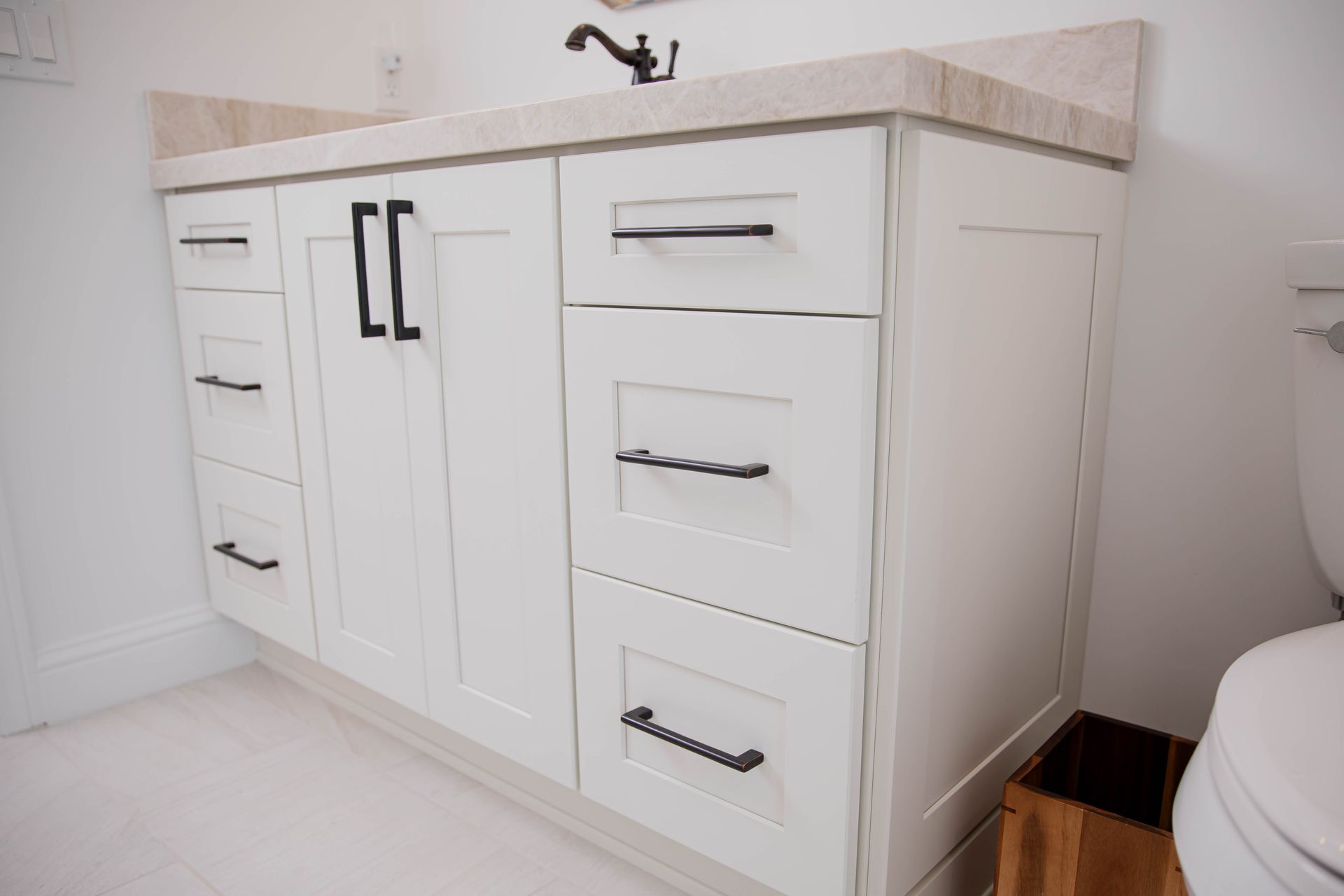 A bathroom vanity with white cabinets and black handles next to a toilet.