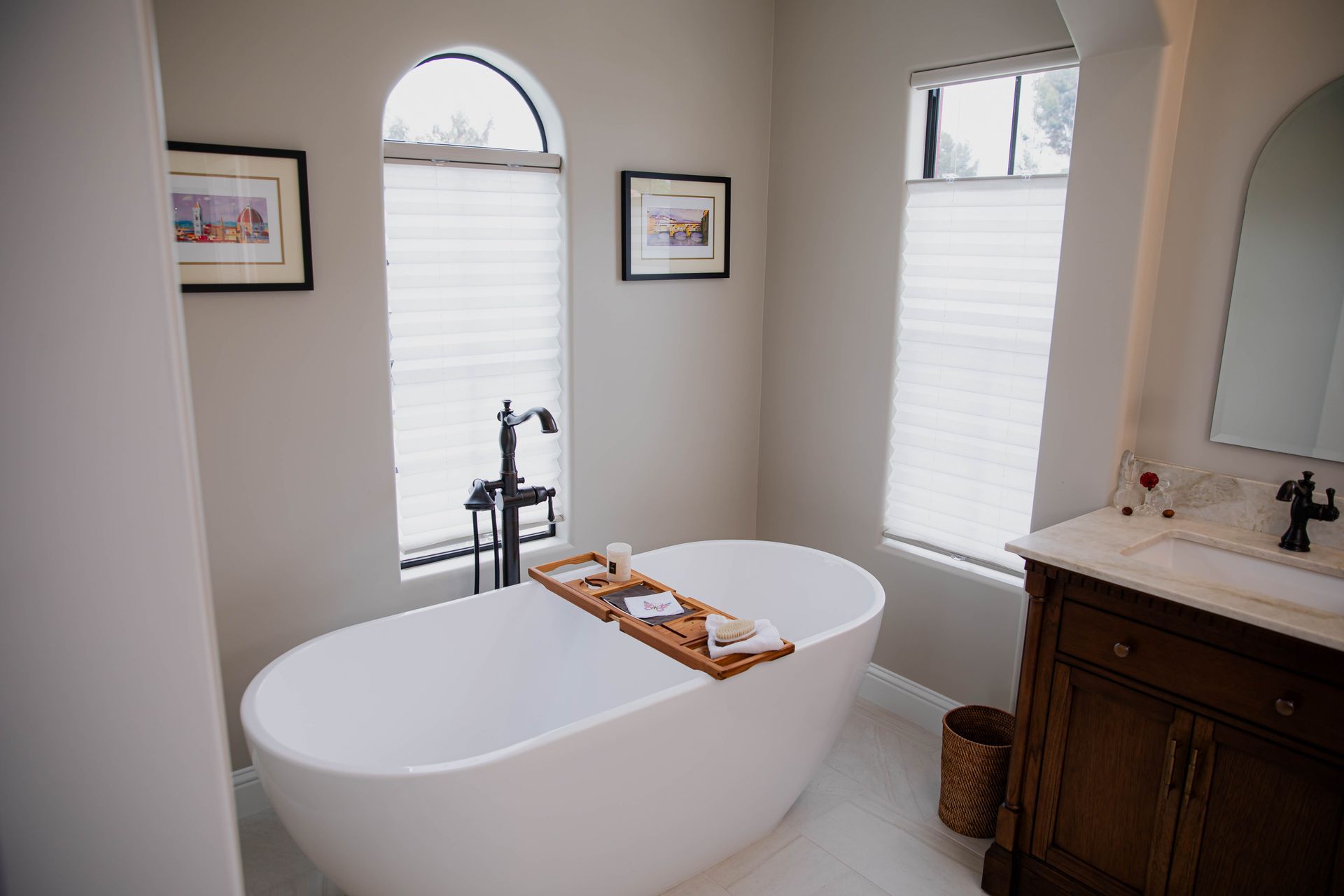 A remodeled bathroom with a bathtub , sink , mirror and two windows.