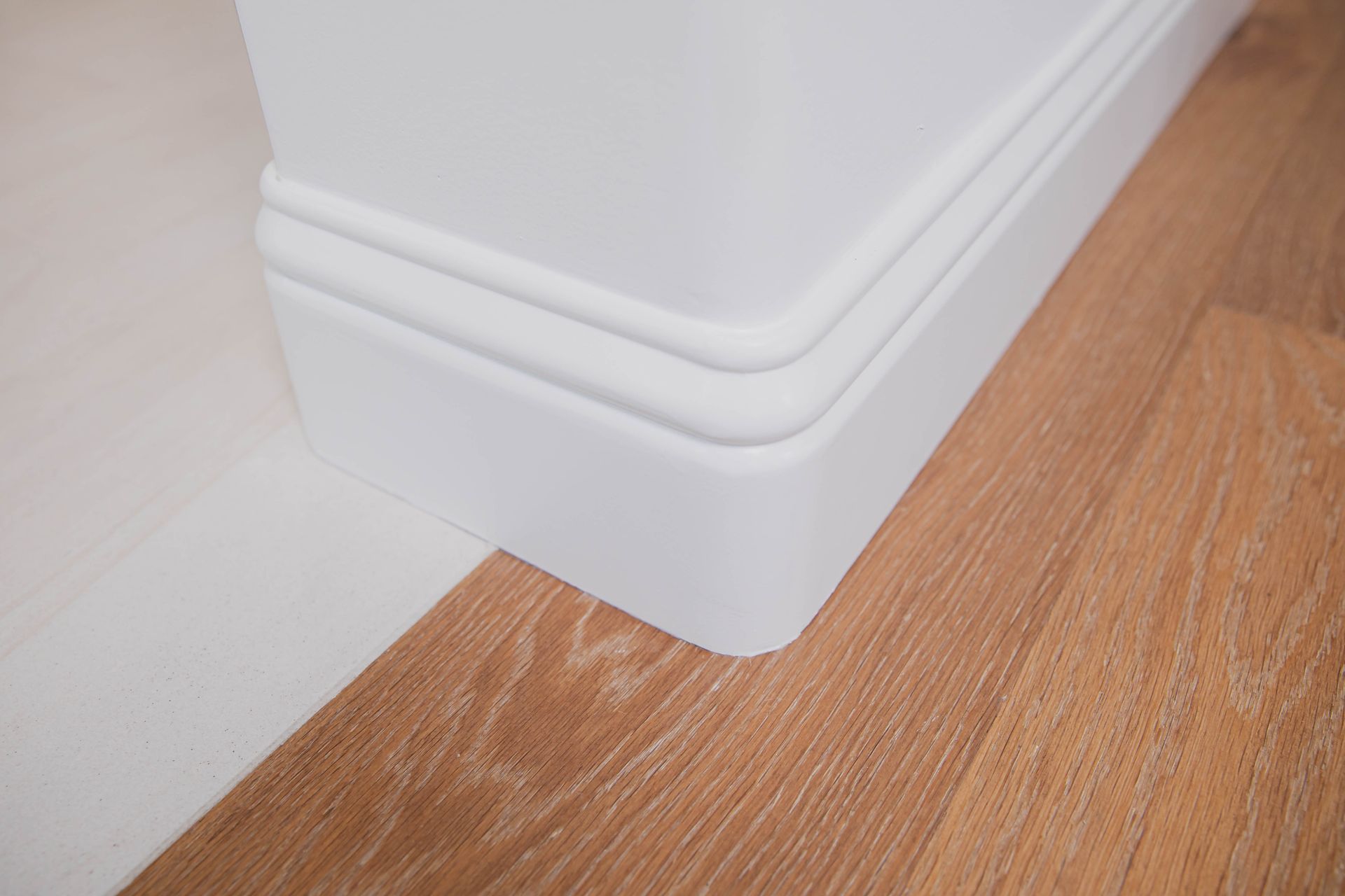 A close up of a white skirting board on a wooden floor.
