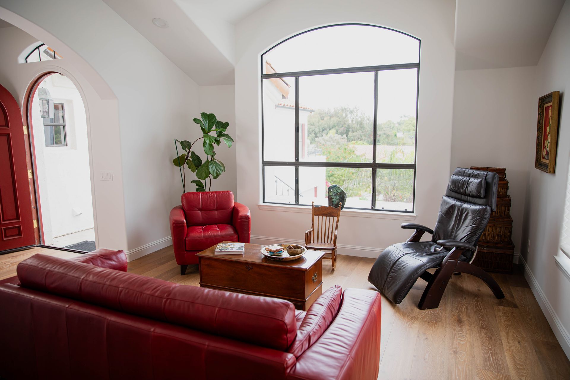 A living room with a red couch , two chairs , a coffee table and a large window.