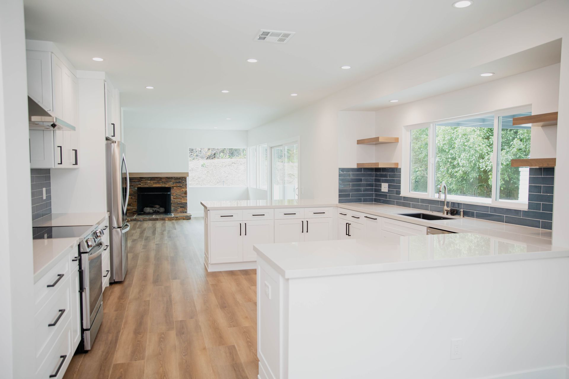 A kitchen with white cabinets , stainless steel appliances , hardwood floors and a fireplace.