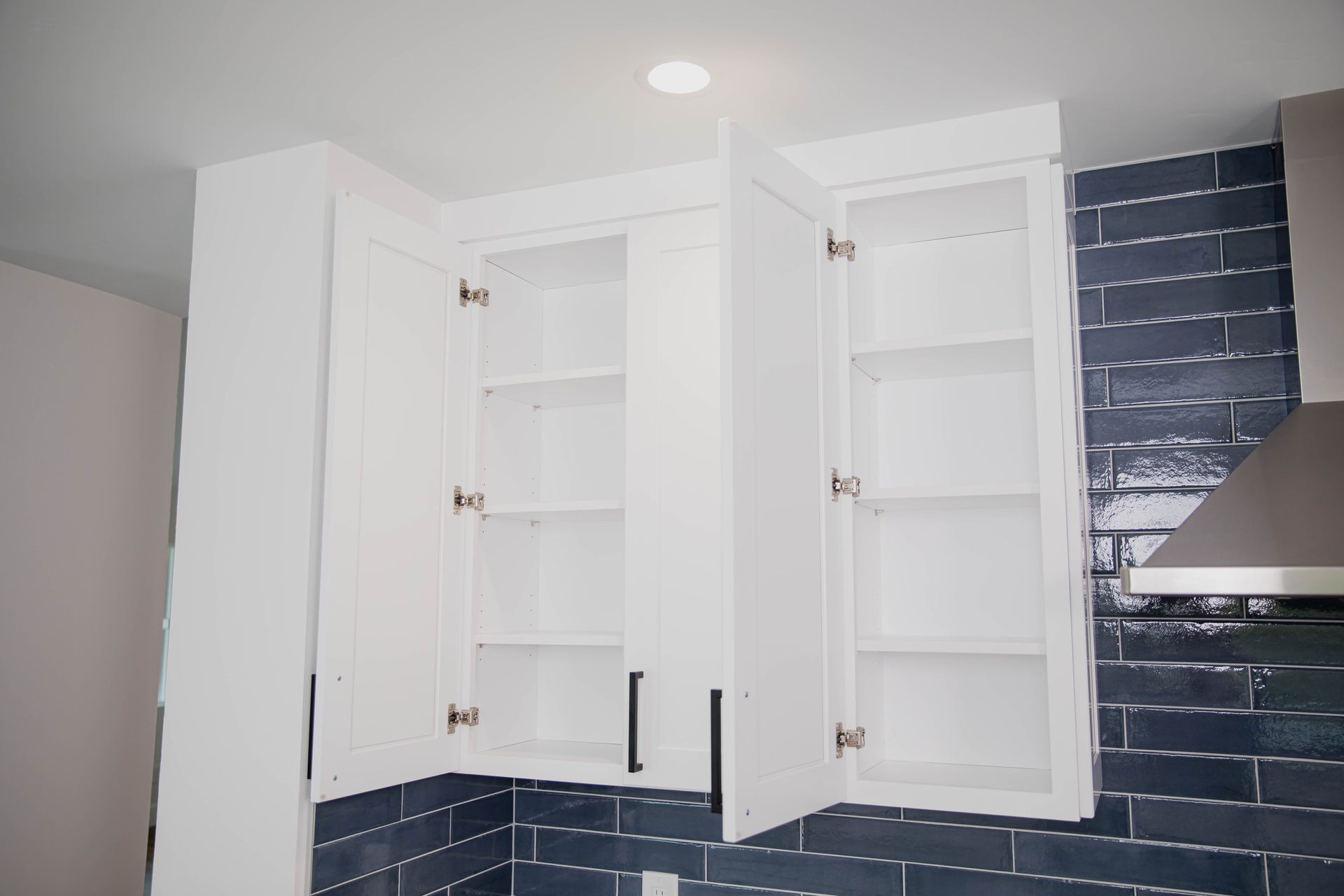A kitchen with blue tiles and white cabinets with the doors open.