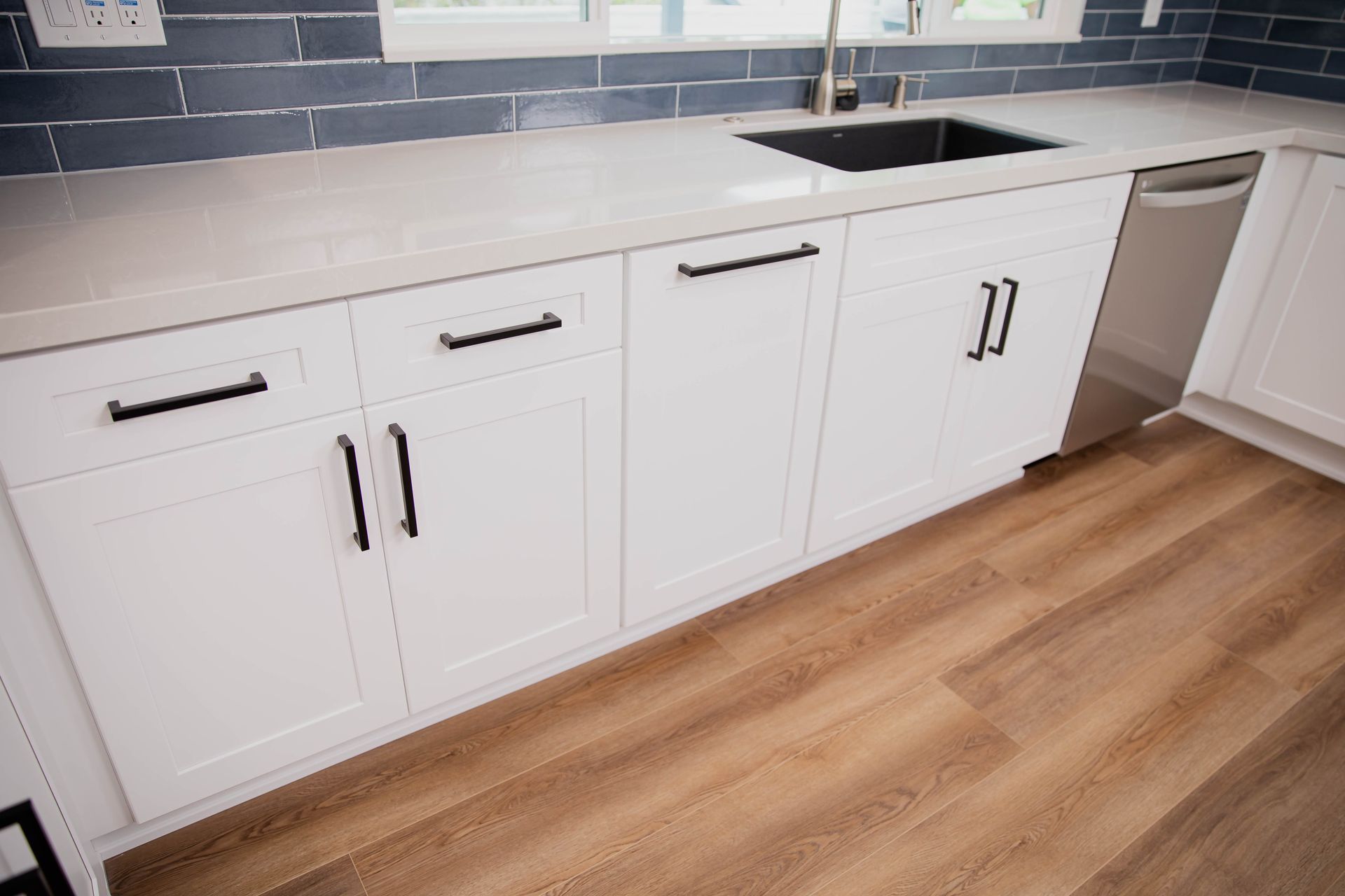 A kitchen with white cabinets , a sink , and a dishwasher.