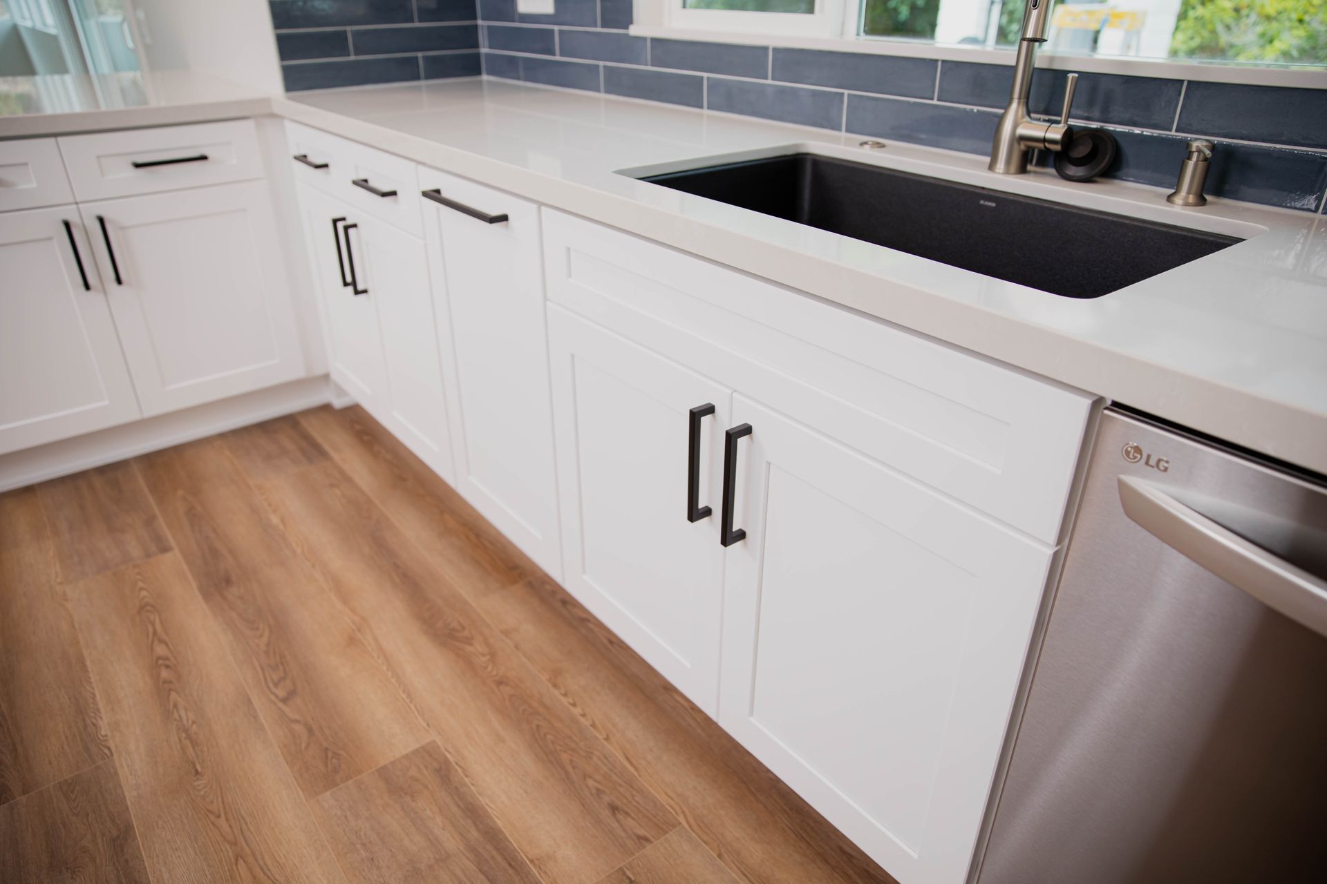 A kitchen with white cabinets , a sink , and a stainless steel dishwasher.