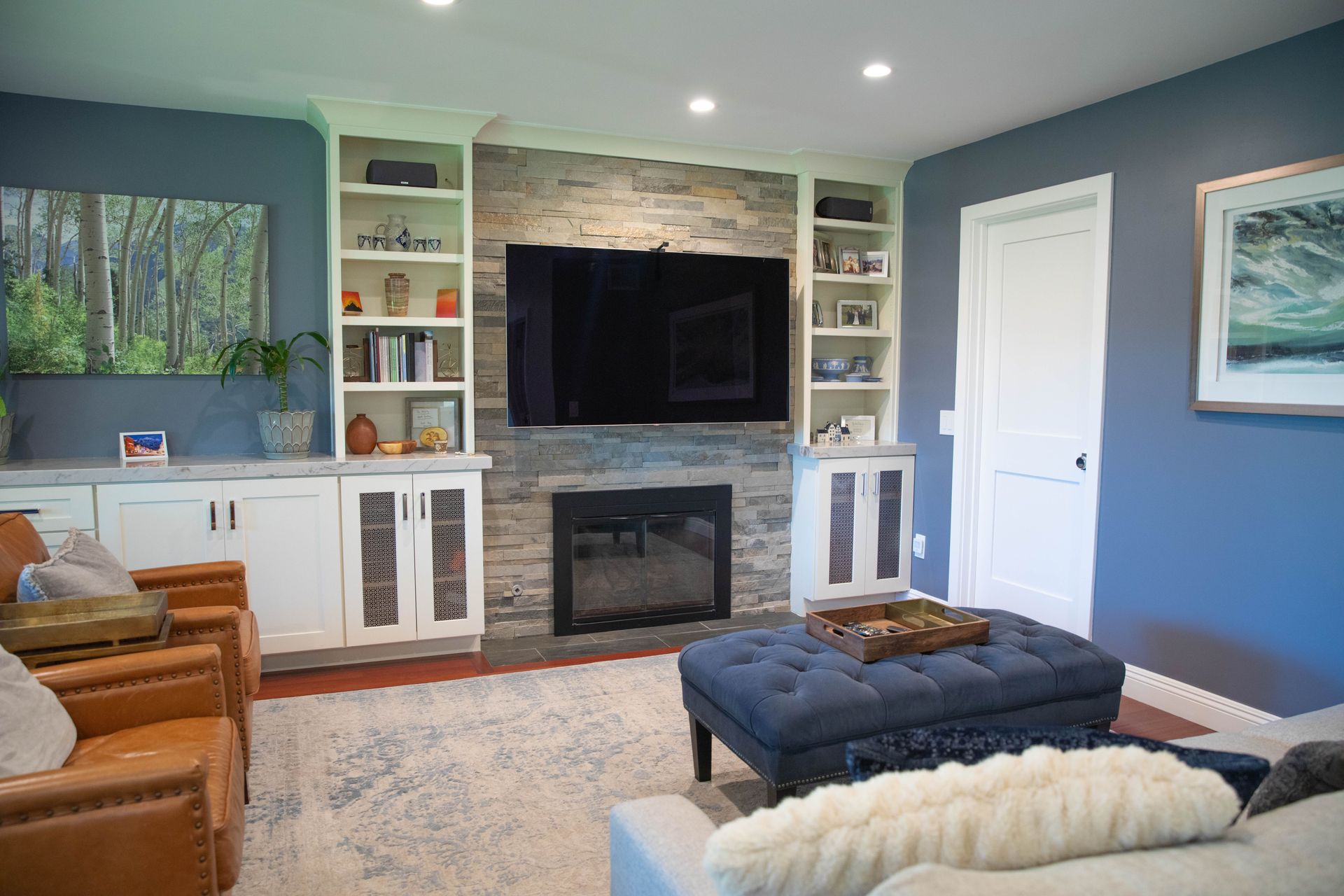 A living room with a couch , chairs , ottoman , television and fireplace.