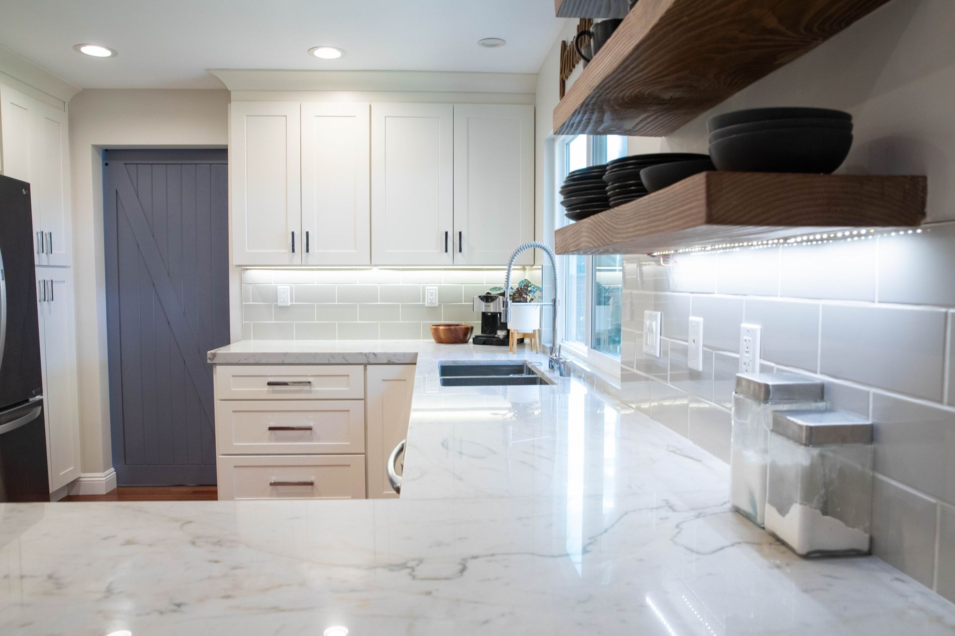 A kitchen with white cabinets , marble counter tops , and a black refrigerator.