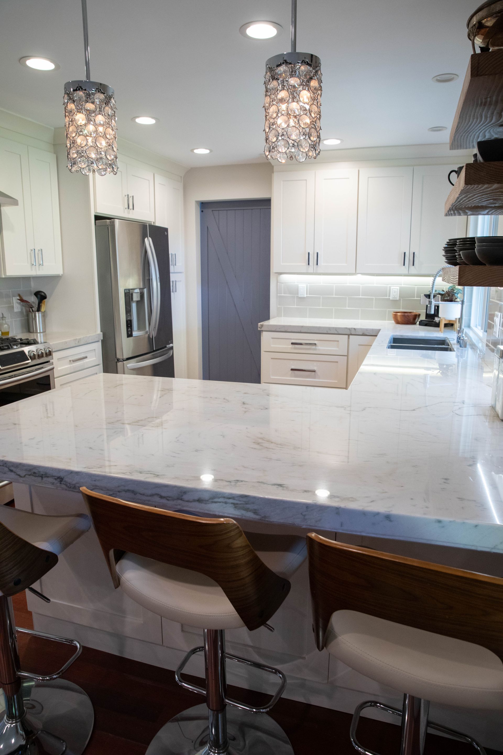 A kitchen with white cabinets and stools and a large counter top.