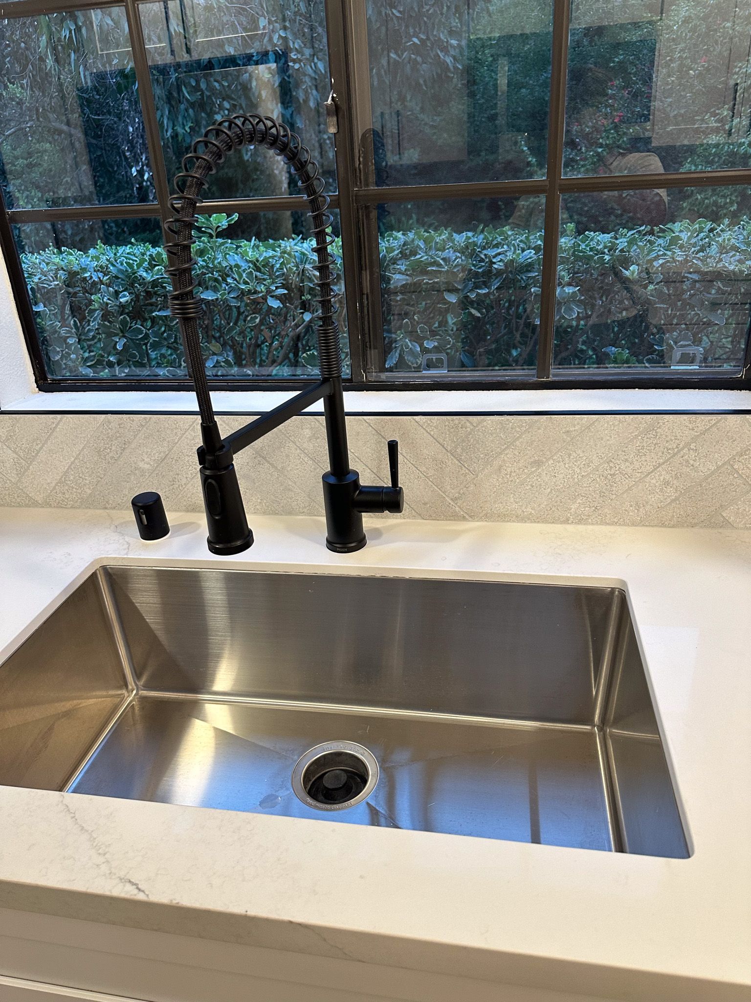 A kitchen sink with a black faucet and a window in the background.