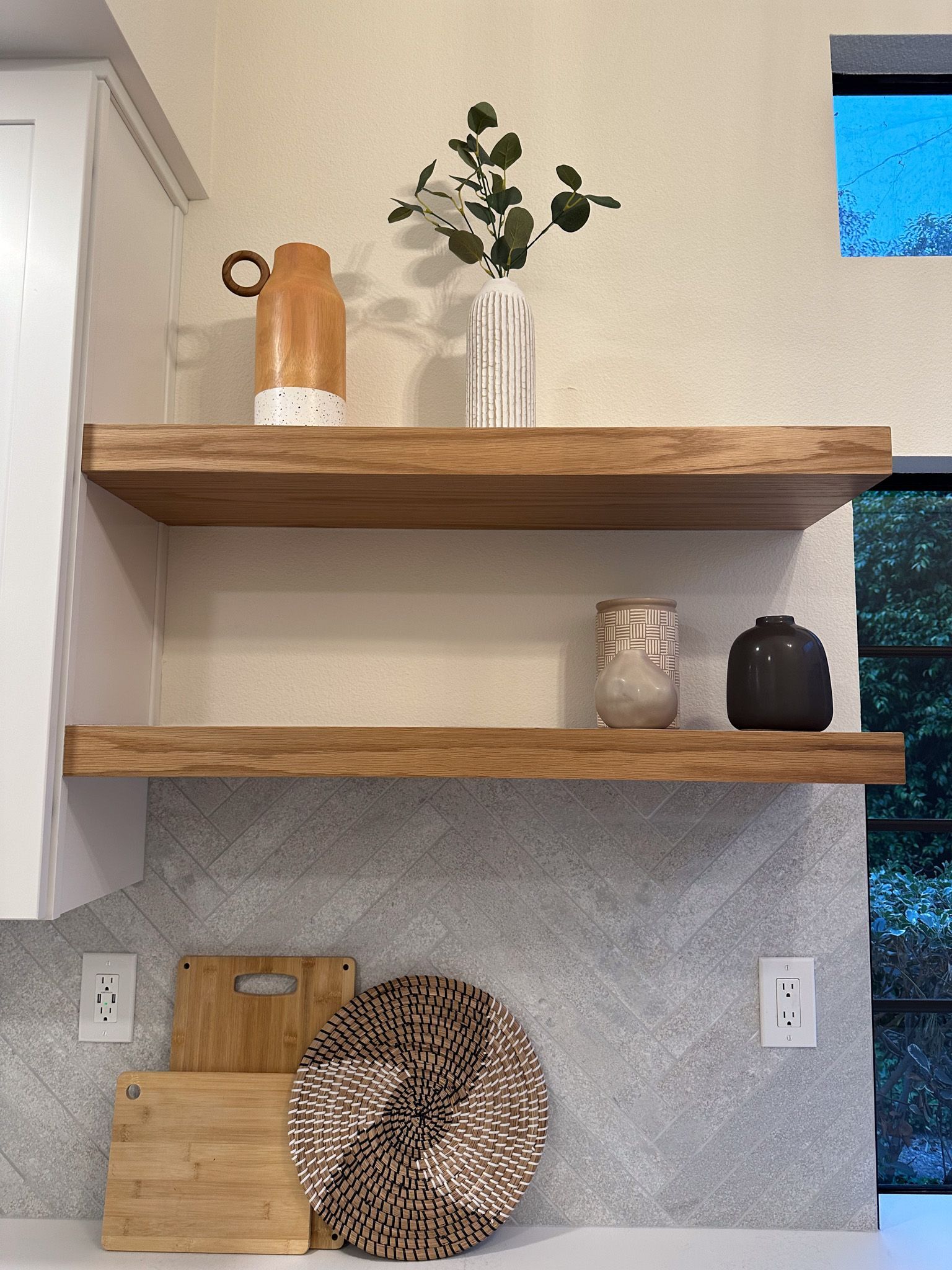 A kitchen with two wooden shelves filled with vases and cutting boards.