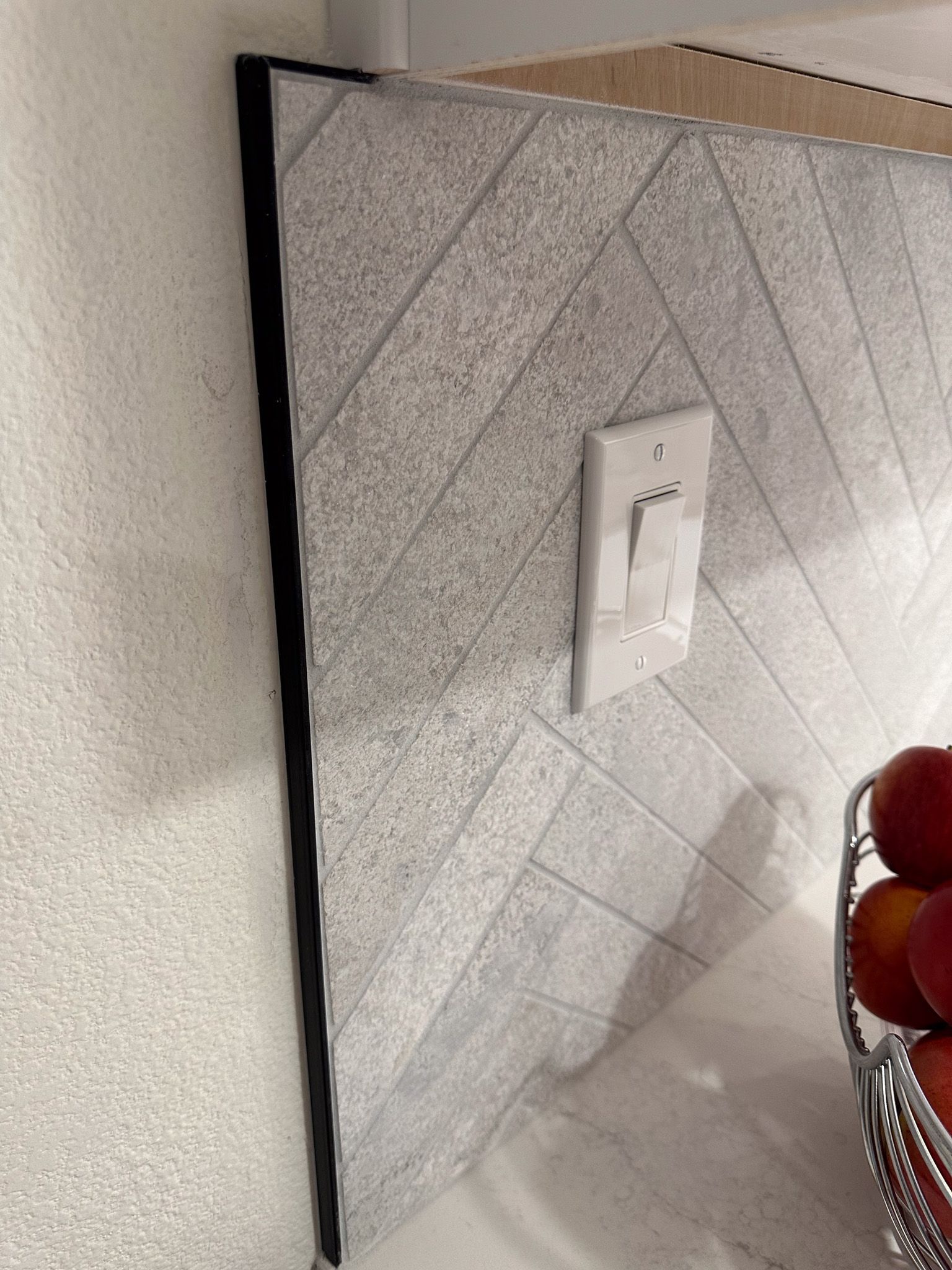 A kitchen counter with a basket of apples and a light switch.