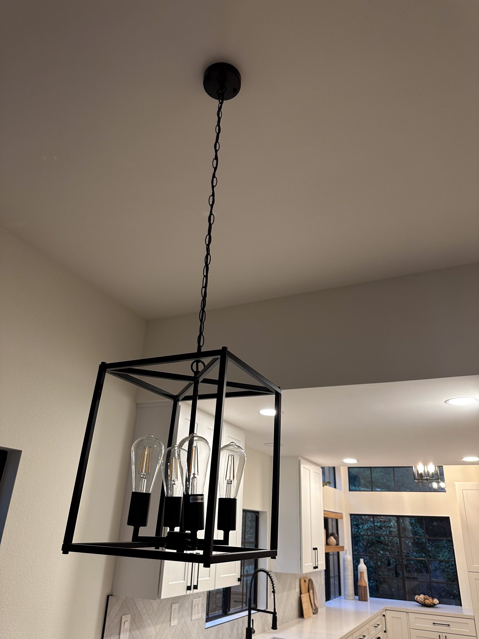 A black chandelier is hanging from the ceiling in a kitchen.
