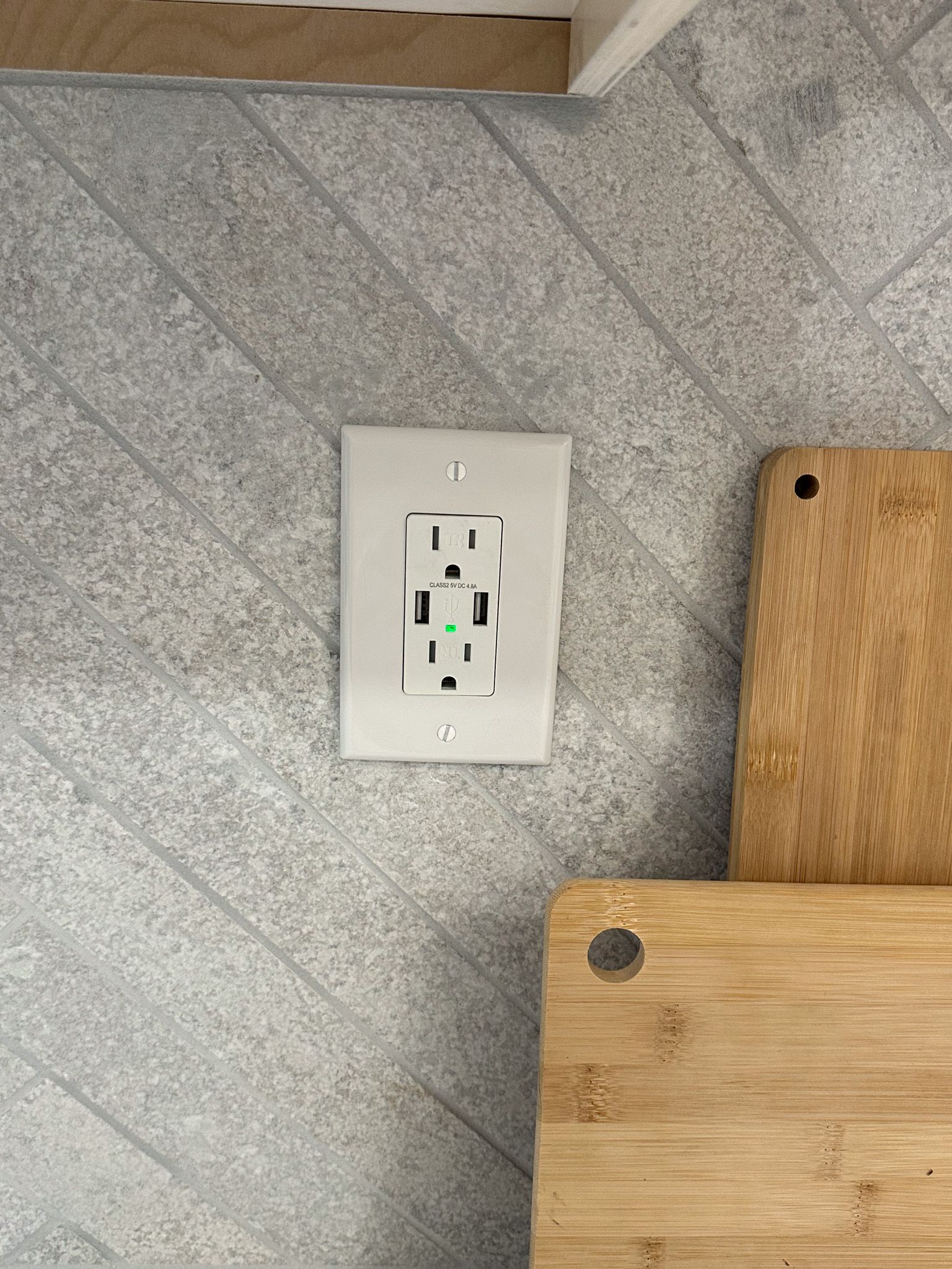 A white electrical outlet on the wall next to a wooden cutting board.