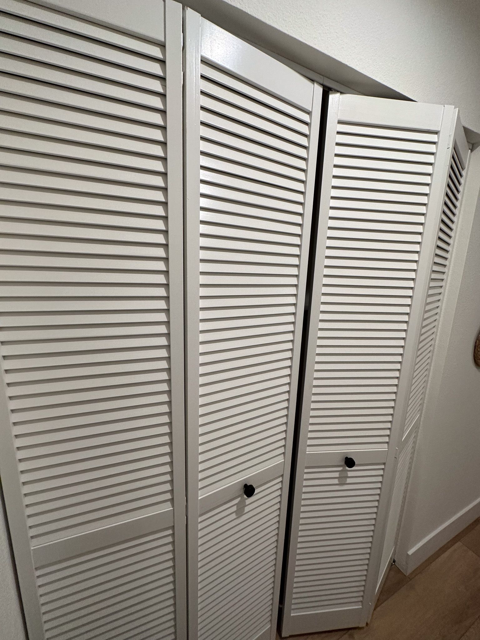 A closet with white shutters and a broken door.
