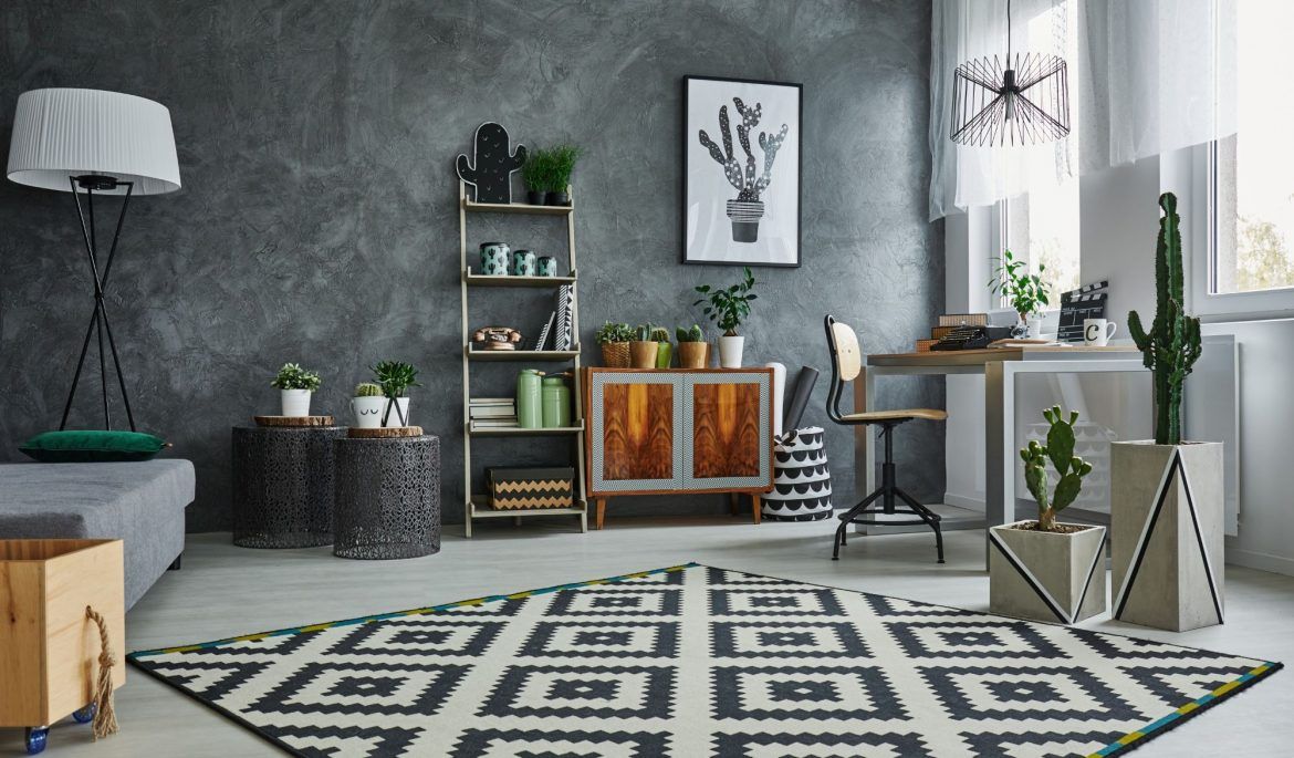 Uma sala de estar com um tapete, um sofá, uma escrivaninha e um cacto na parede.