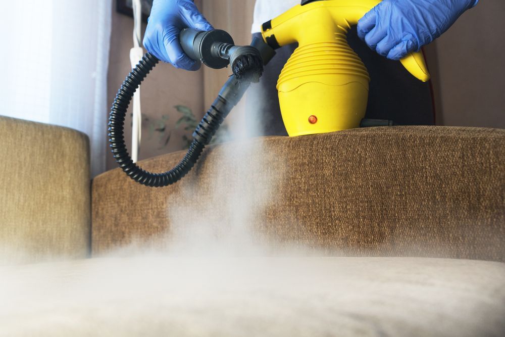 Uma pessoa está limpando um sofá com um limpador a vapor.