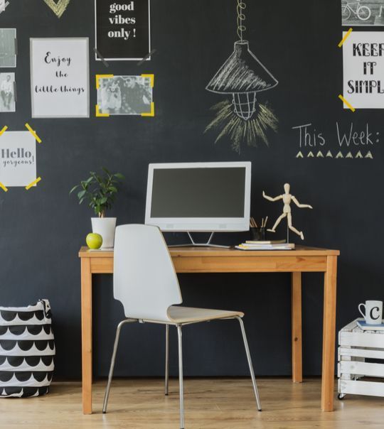 Uma mesa com um computador e uma cadeira em frente a um quadro negro que diz esta semana