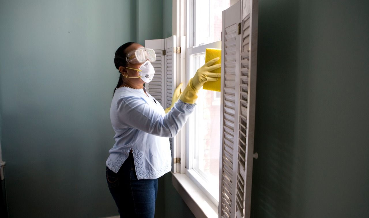 Uma mulher usando máscara e luvas está limpando uma janela.