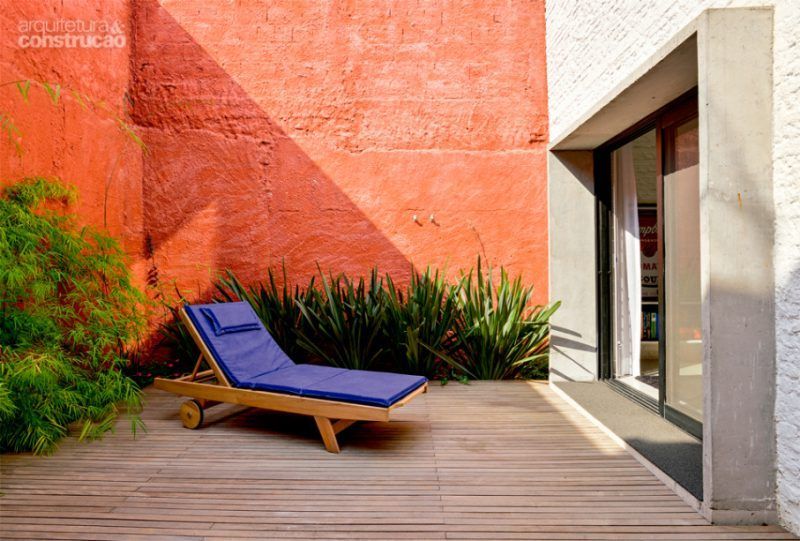 Uma poltrona azul está sobre um deck de madeira em frente a uma parede de tijolos vermelhos.