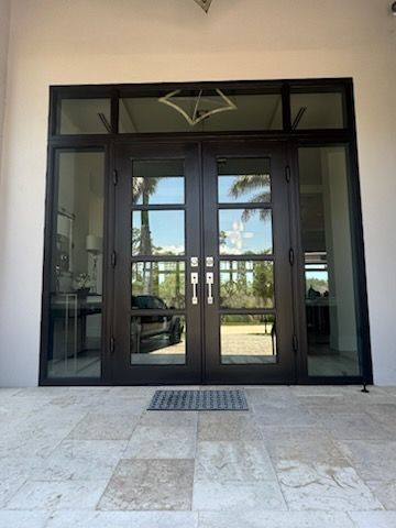 Brown wooden front door with ornate metal window, on a tan building exterior with a porch.