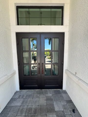Black front door with small window, brass handle, set in a stone archway with bushes.